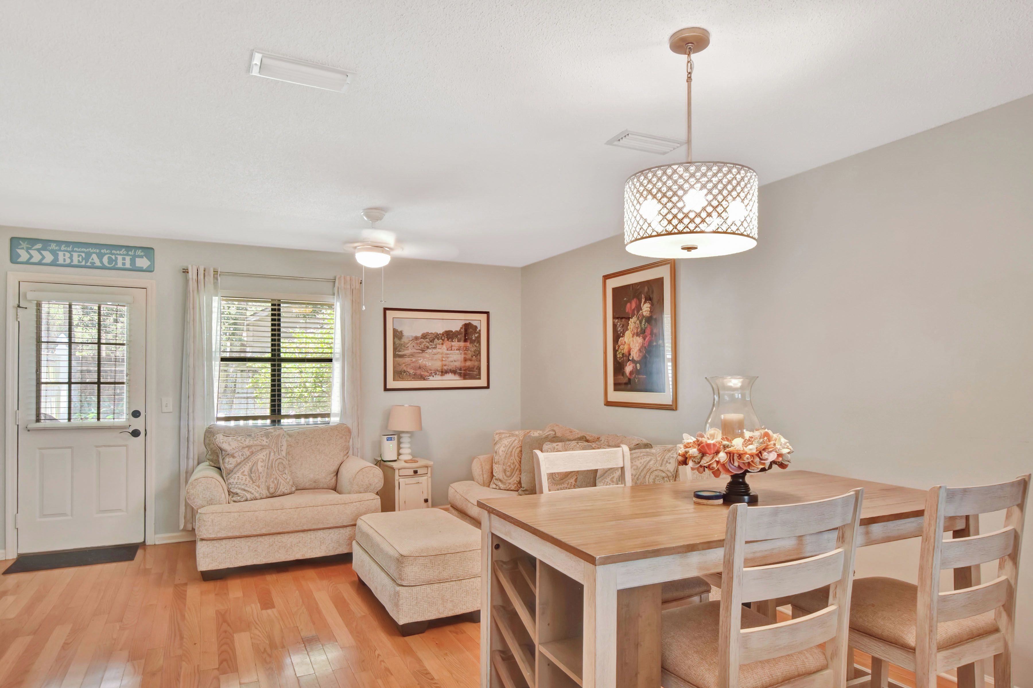 A cozy living room with a wooden dining table, cushioned seating, a ceiling fan, and a decorative lamp.
