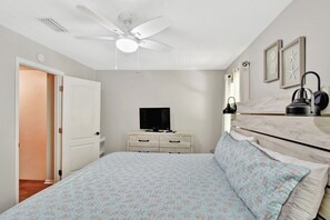 Quarto com cama, ventoinha no teto, cômoda, televisão e mesa de cabeceira.