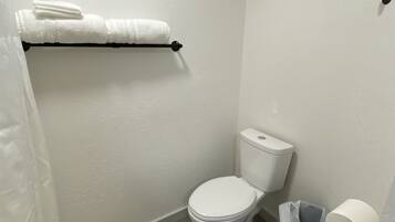 A small bathroom with a toilet, a towel rack with towels, a trash bin, and a toilet paper holder.