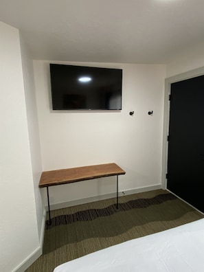 Ein Hotelzimmer mit einem wandmontierten Flachbildfernseher, einer hölzernen Bank und einer Tür.