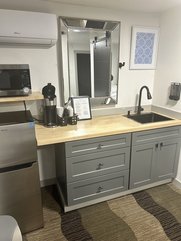 A compact kitchenette with a microwave, coffee maker, and a framed welcome sign.