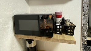 Eine Küche mit einer Mikrowelle, einer Kaffeemaschine und einem Regal mit Küchenutensilien.