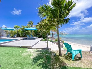 A pool area with lounge chairs and umbrellas, a palm tree, and a view of the ocean. - Luxury villa · St-François · Sea view & beach access (Saint-François)