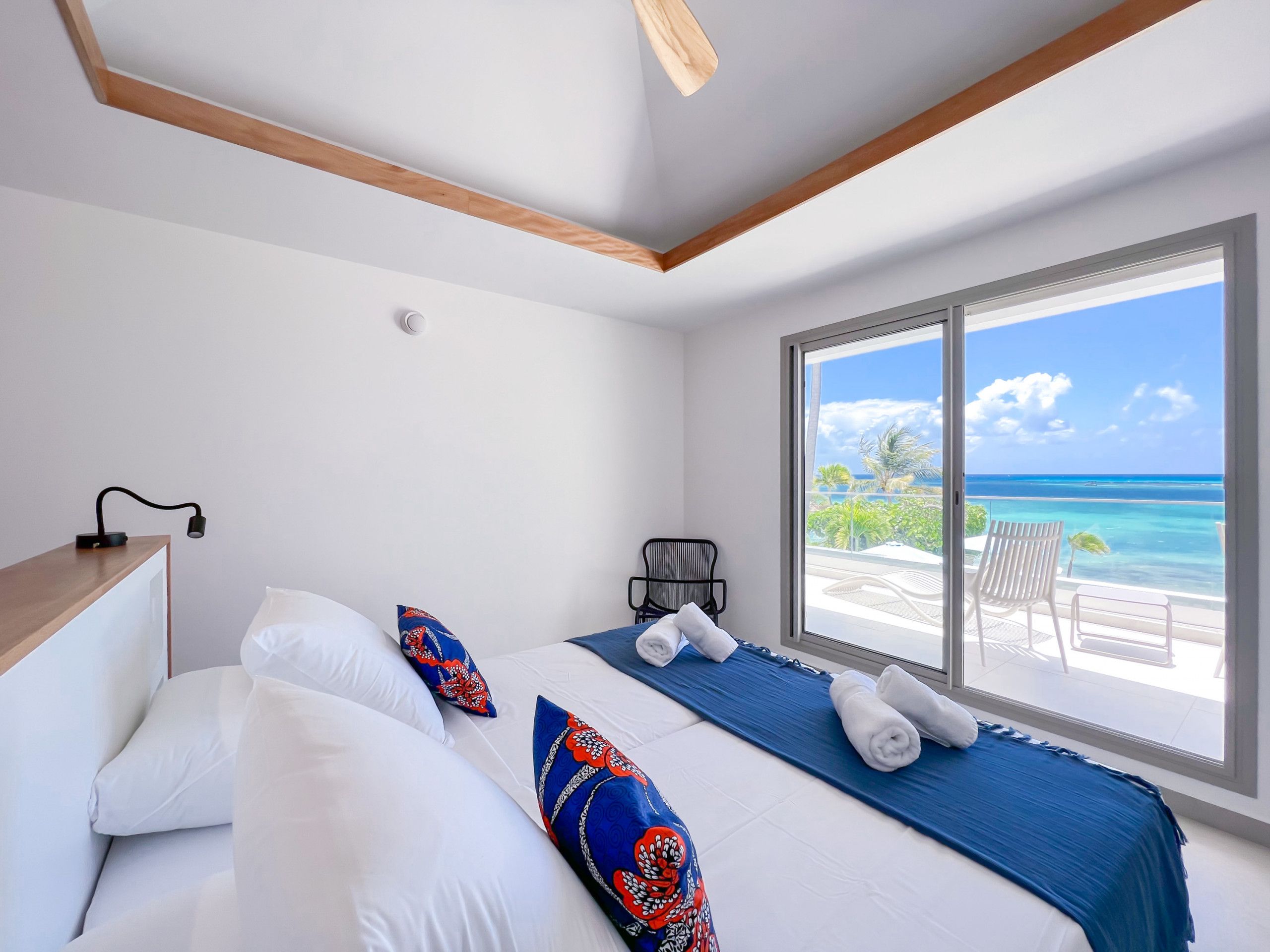 A hotel room with a bed, a desk, a chair, and a large window with a view of the ocean.