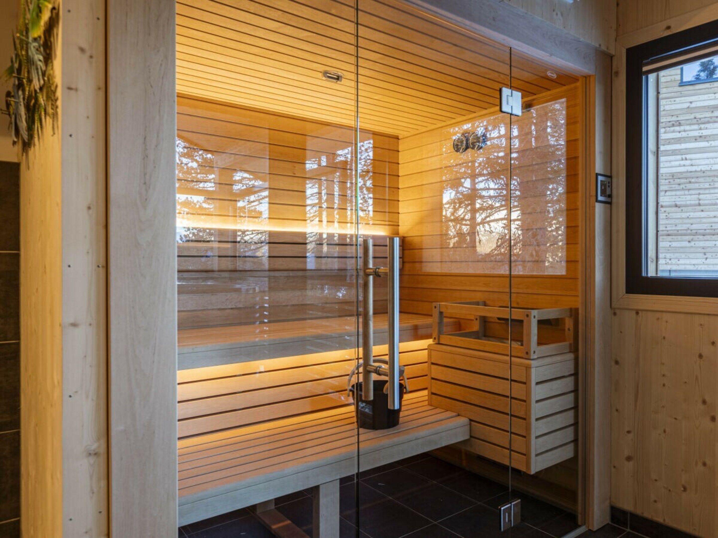 Un sauna avec des bancs en bois et une porte en verre, doté d’un plafond en bois et d’une fenêtre.