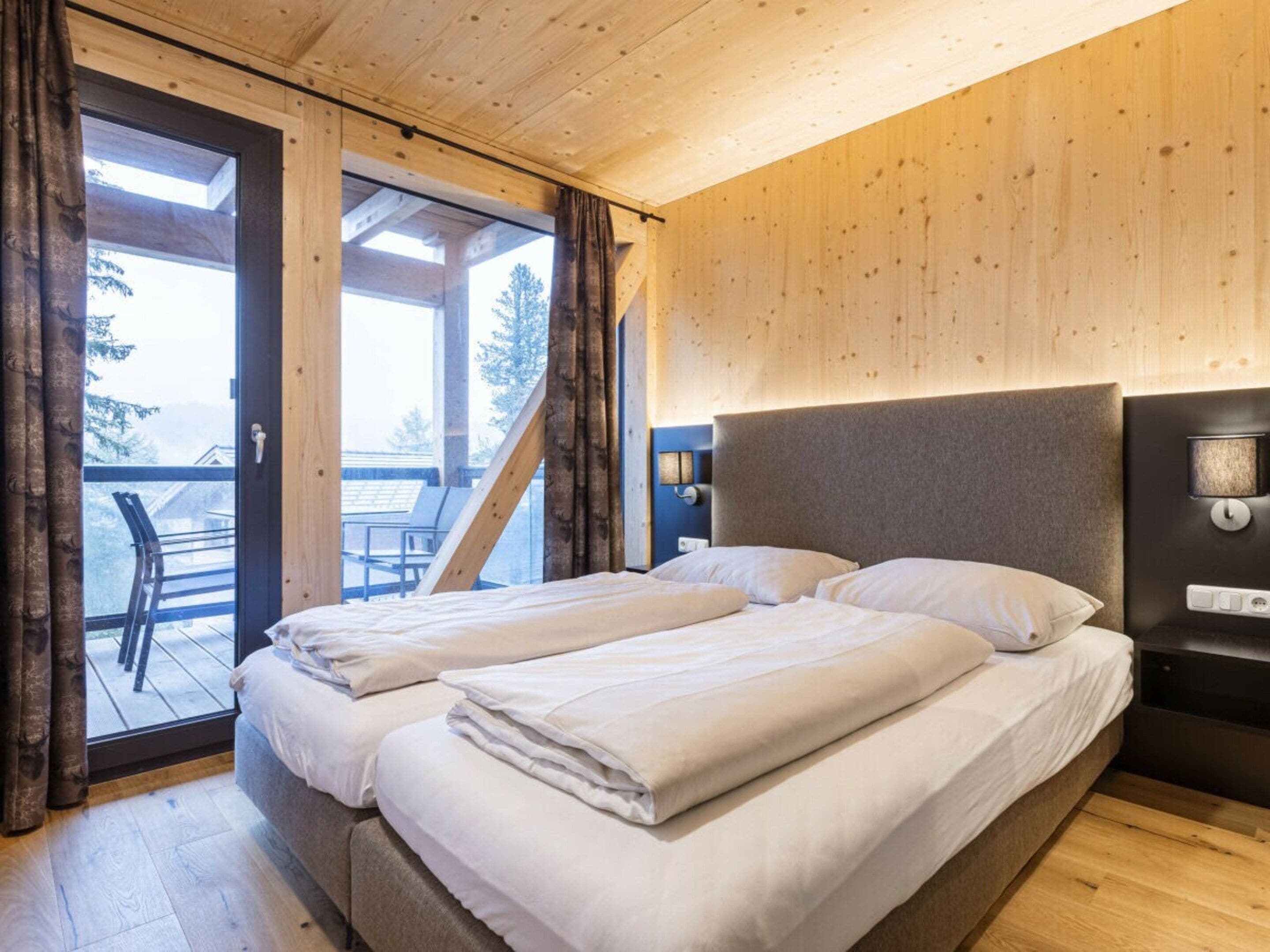 A double bed with a headboard, a bedside table with a lamp, and a view of the outdoors through a glass door.