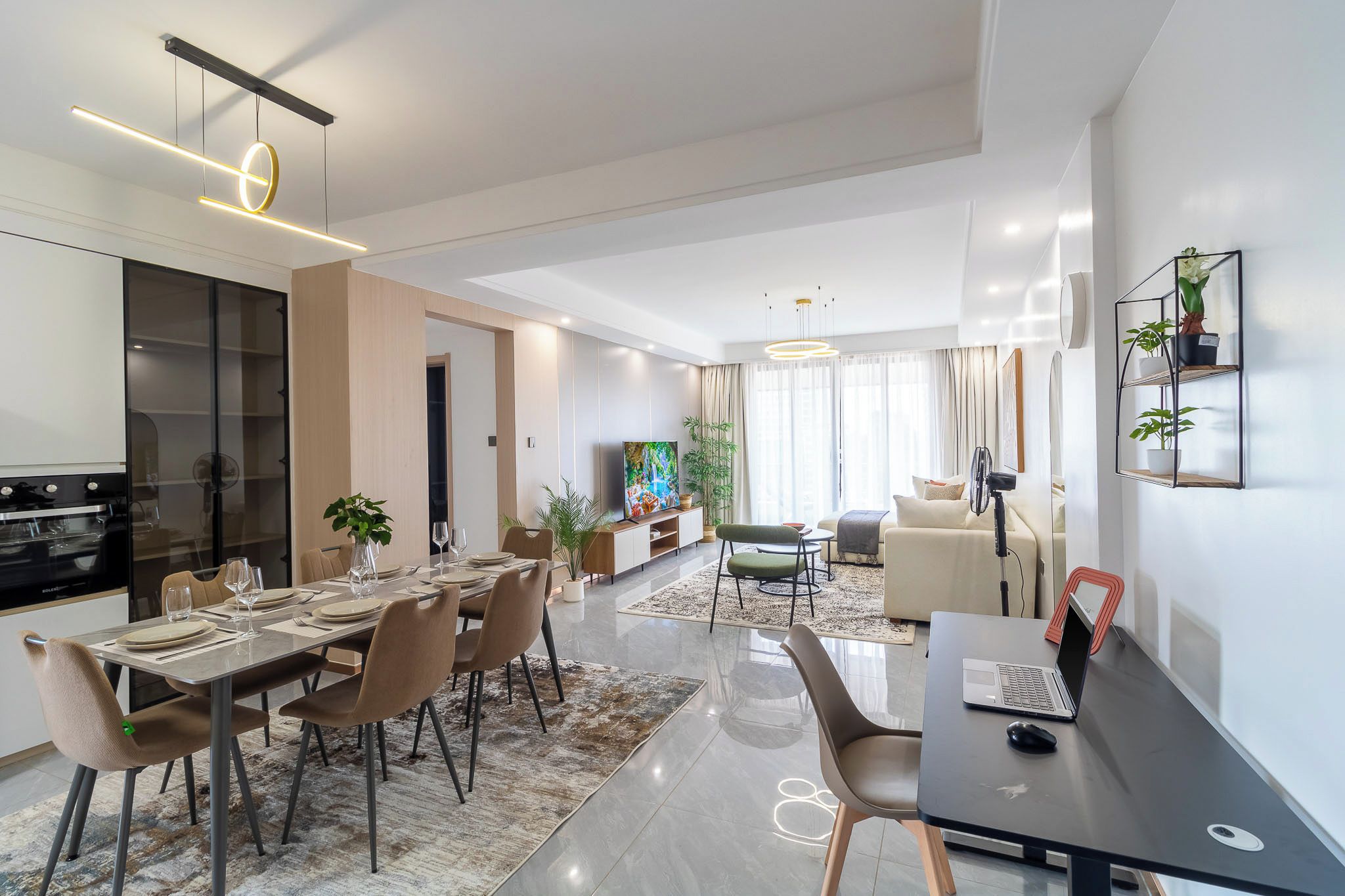 Un soggiorno moderno con divano, un'area pranzo con tavolo imbandito per quattro persone e una cucina con piano cottura.