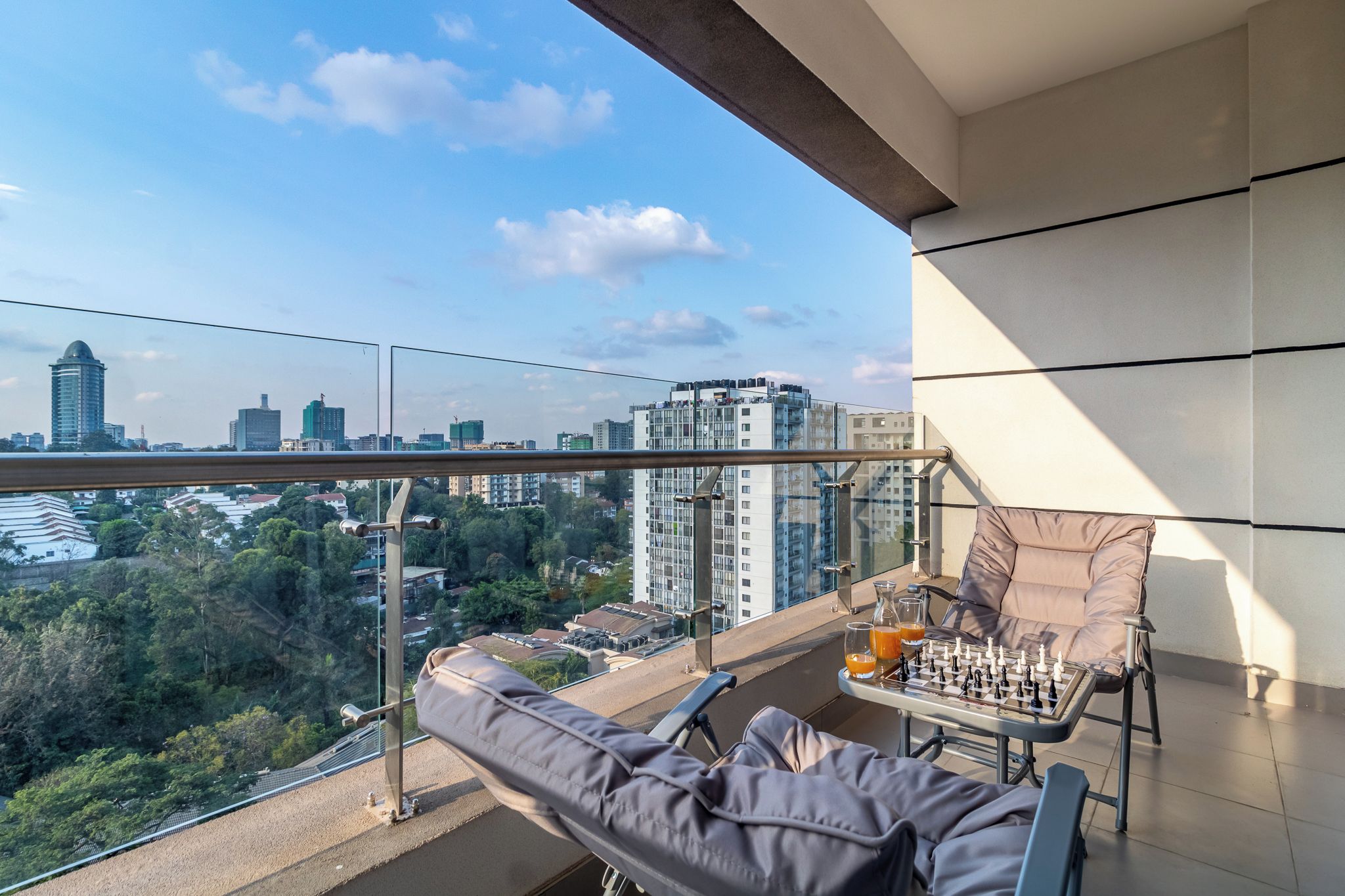 A balcony with a chessboard, two glasses of orange juice, and a cushioned chair.