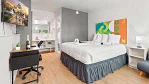 A hotel room with a bed, desk, chair, TV, and artwork. - Hotel-Style Room Pool, Disney Shuttle (Kissimmee)