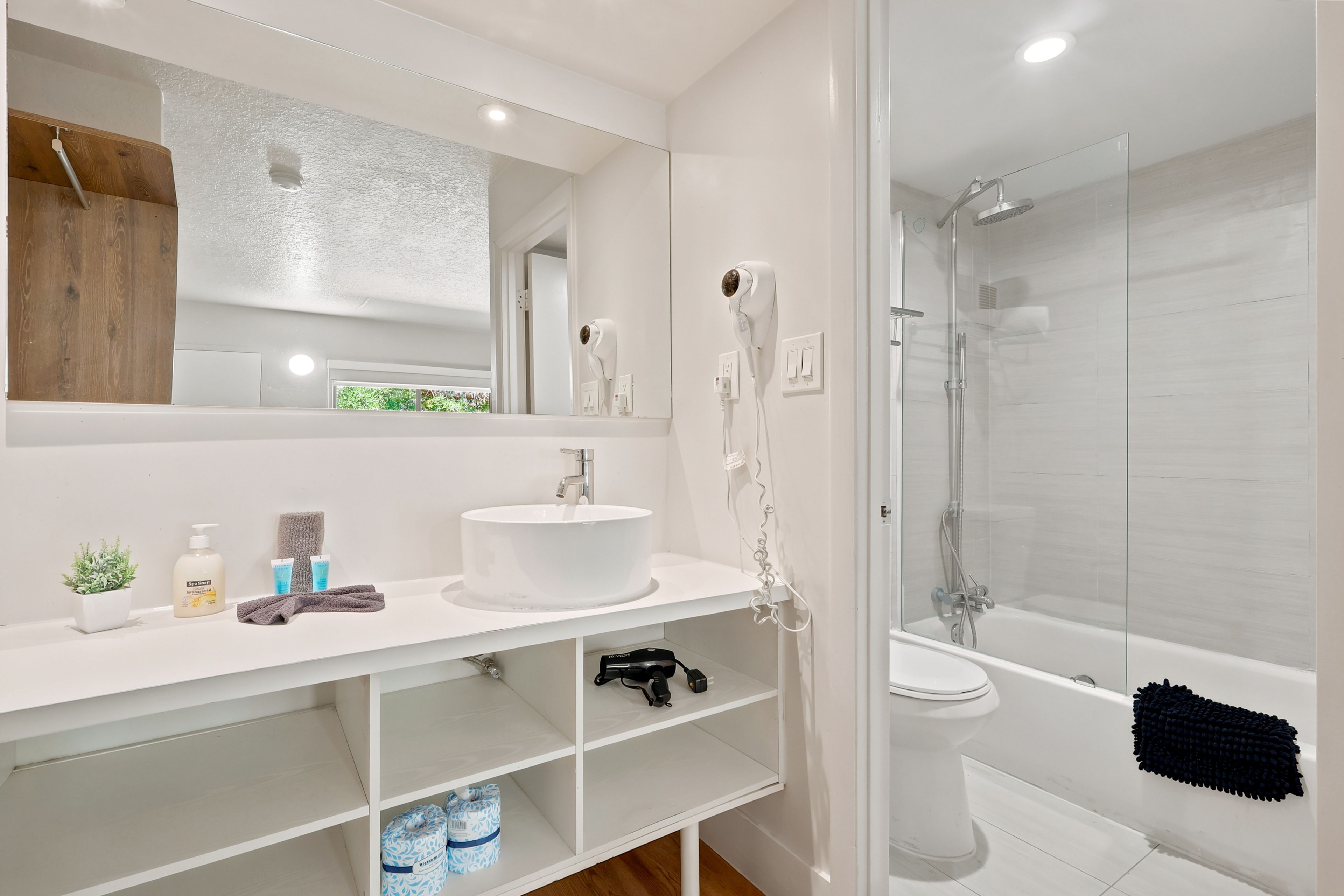 A modern bathroom with a white sink, mirror, and glass shower enclosure.
