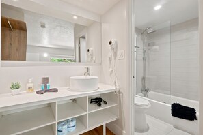 A modern bathroom with a white sink, mirror, and glass shower enclosure. - Hotel-Style Room Pool, Disney Shuttle (Kissimmee)