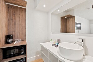 A modern bathroom with a white sink, a large mirror, a wooden shelf with a coffee maker, and a microwave. - Hotel-Style Room Pool, Disney Shuttle (Kissimmee)