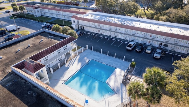 An aerial view of a hotel with a swimming pool, parking area, and adjacent buildings. - Hotel-Style Room Pool, Disney Shuttle (Kissimmee)