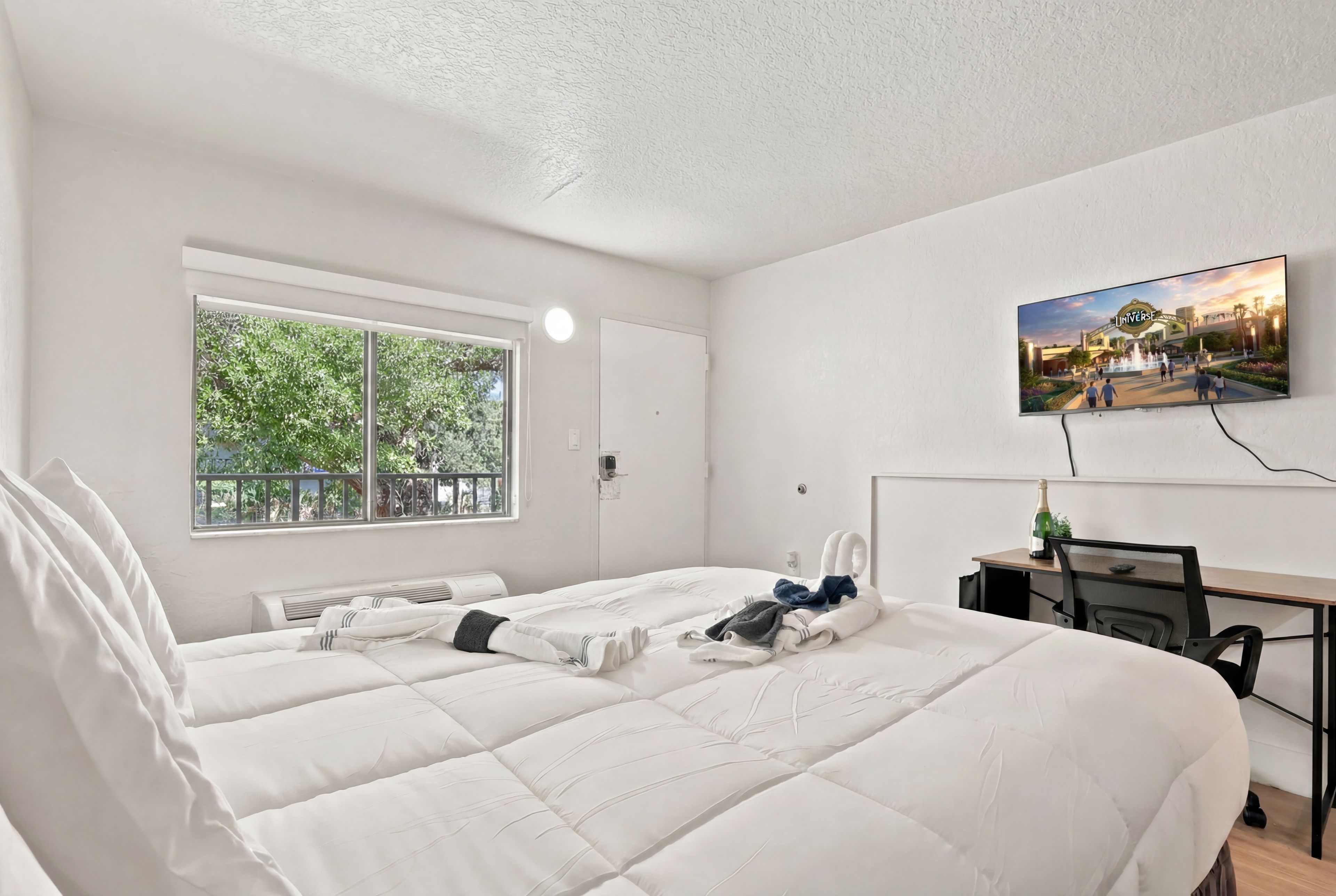 Une chambre d’hôtel avec deux lits, un bureau, une chaise, une télévision et une fenêtre donnant sur un paysage verdoyant.