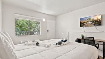 Une chambre d’hôtel avec deux lits, un bureau, une chaise, une télévision et une fenêtre donnant sur un paysage verdoyant.