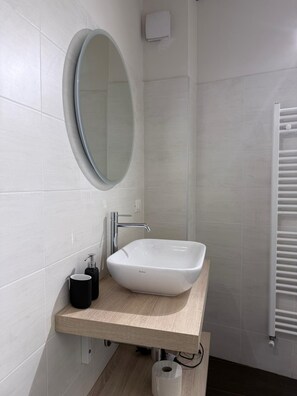 A bathroom with a white sink, a round mirror, and a towel rack. - Ametista | Urban Suite (Valenza)