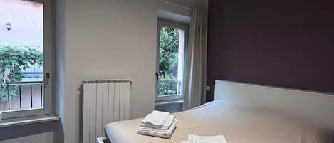 Un dormitorio moderno con una cama grande, dos ventanas, un radiador y una lámpara en el techo.