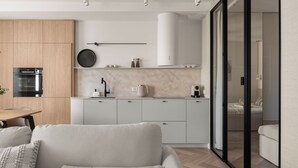 A modern kitchen with a built-in oven, a dining area with a table and chairs, and a living room with a sofa. - Wilcza Premium Residence with parking (Gdańsk)