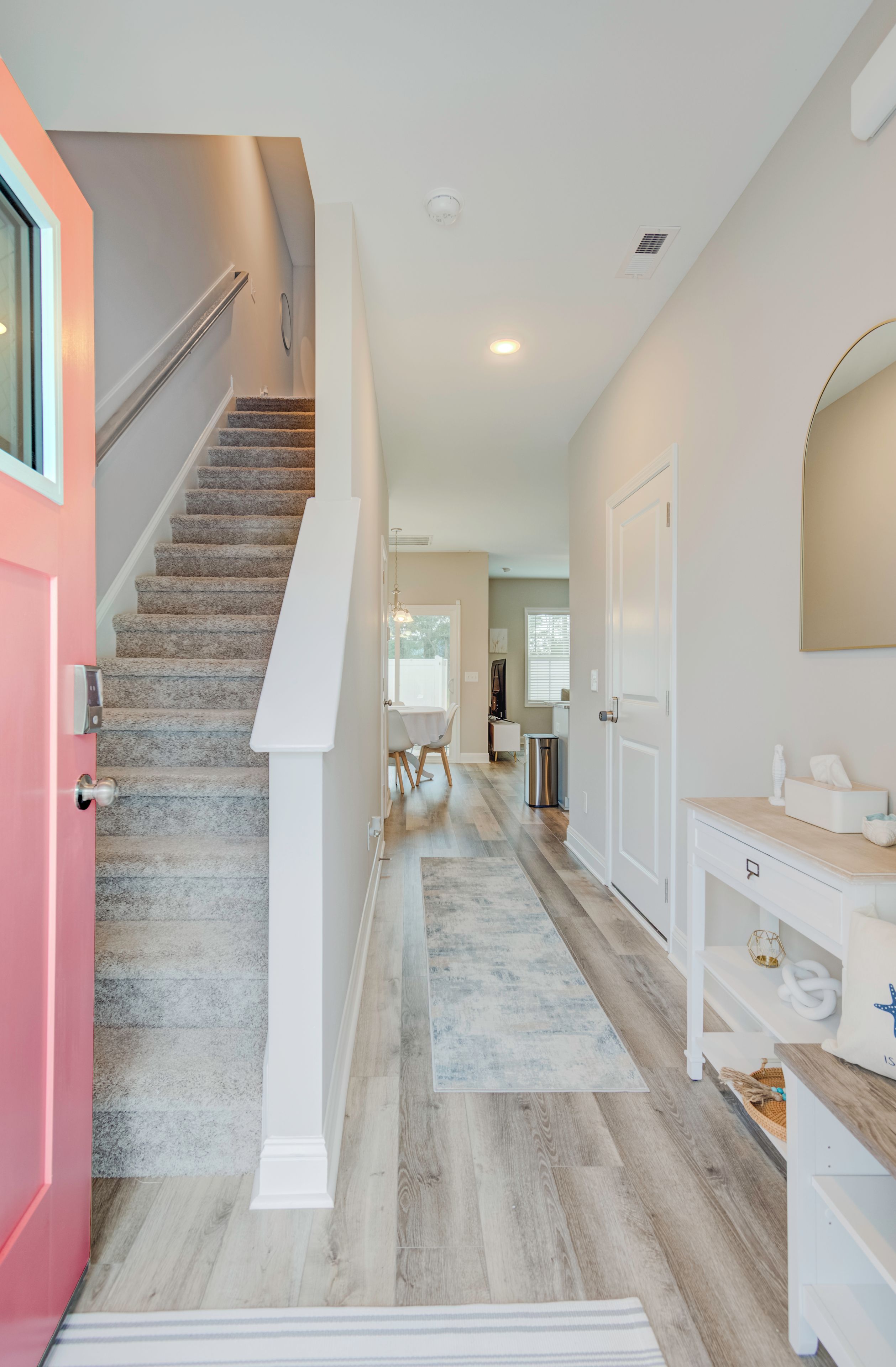 A modern interior with a staircase, a hallway leading to a dining area, and a bathroom with a vanity.