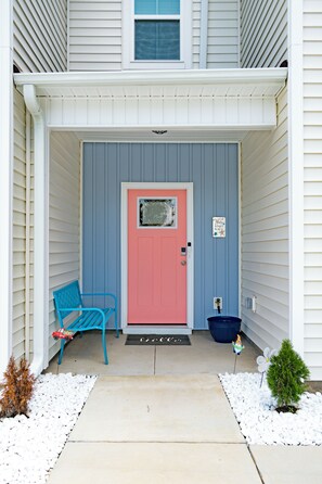 A house with a pink door, a blue chair, and a small gnome statue. - Spacious 3-bedroom townhome in beautiful Cedar Point, NC (Cedar Point)
