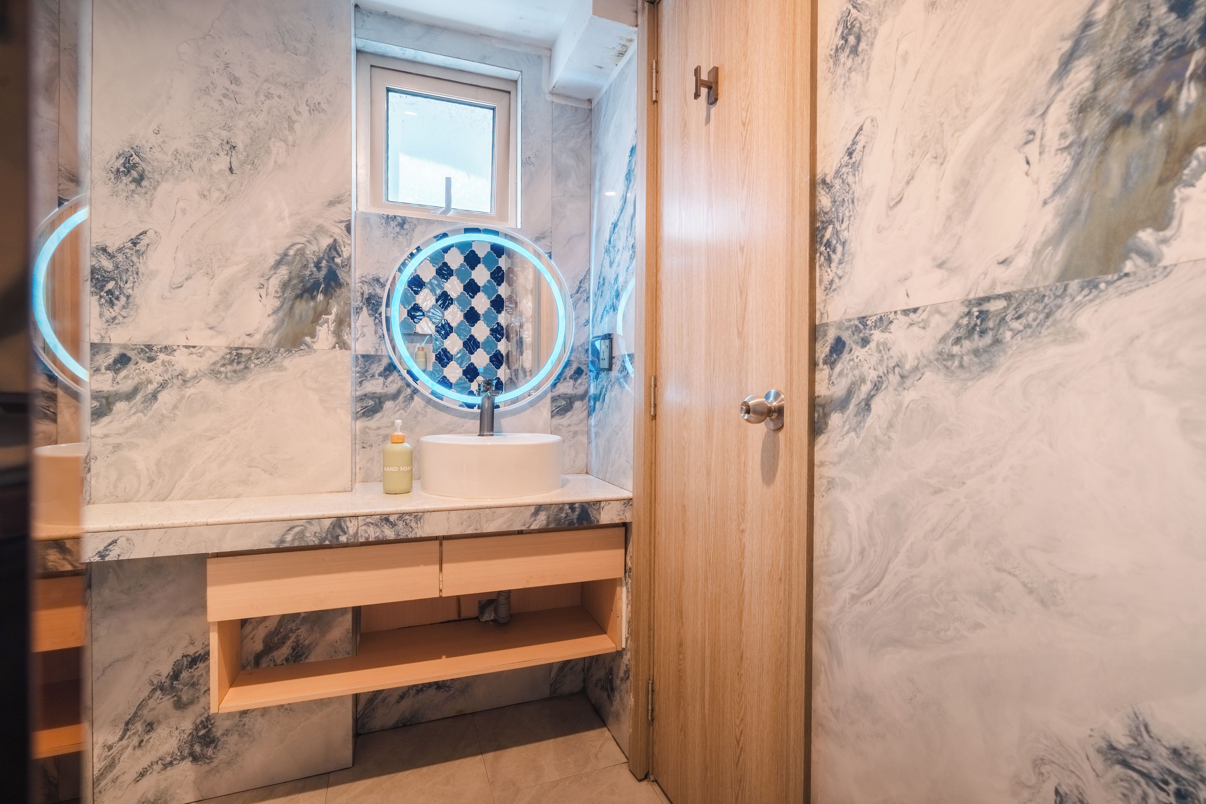 A bathroom with a marble sink, a mirror with a blue light, and a wooden door.