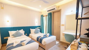 A hotel room with two beds, a desk, a chair, a mirror, and a window with curtains. - Six Palms Beach (Hulhumale)
