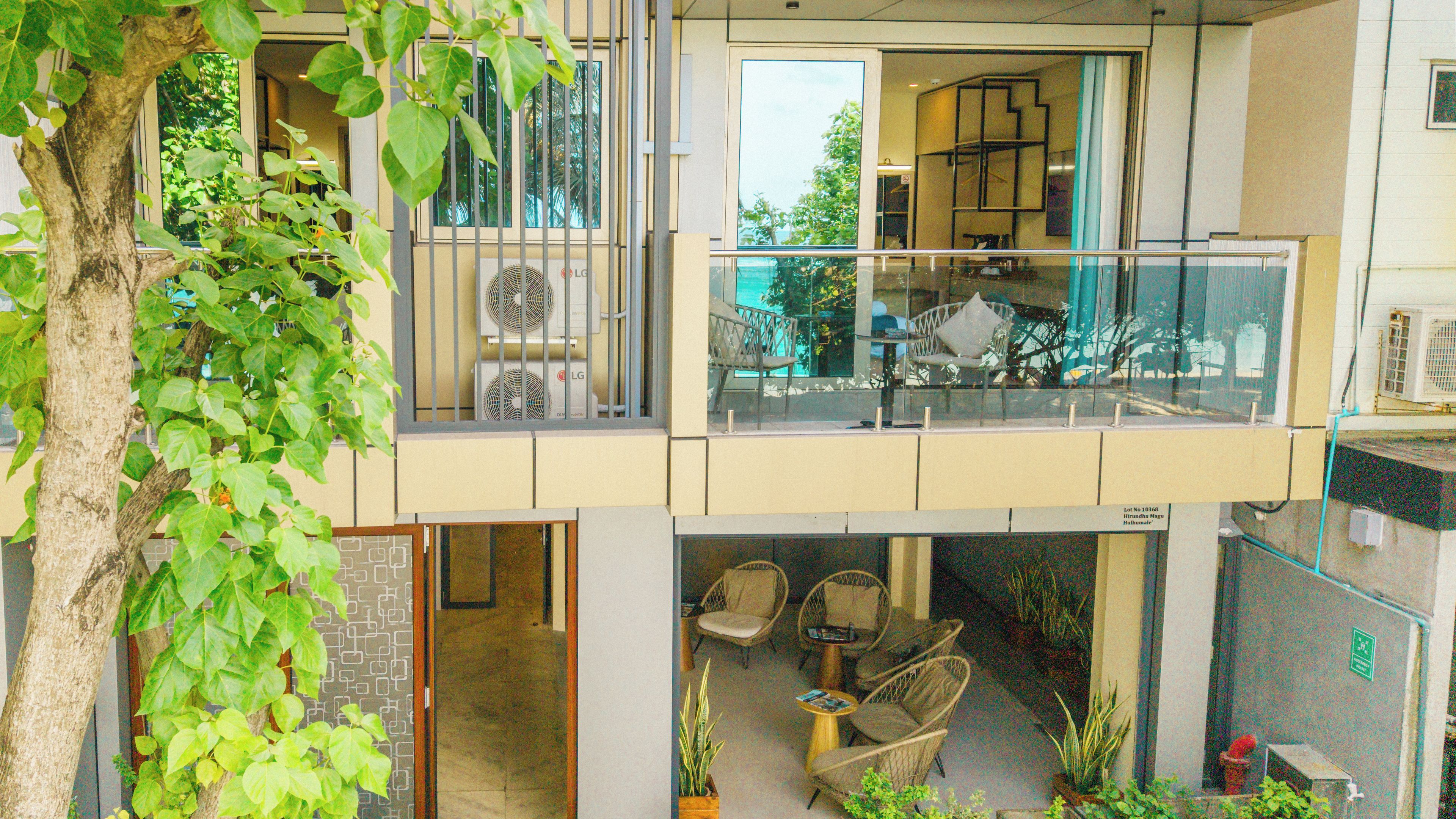 Un edificio de varios niveles con balcón, zona de estar interior y un árbol.