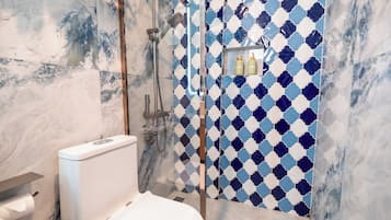 A bathroom with a marble floor, a toilet, a shower with a blue and white patterned wall, and a shelf with toiletries.