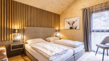 Un dormitorio con pared de listones de madera, una cama con ropa blanca, una mesita de noche con una lámpara y una ventana con vistas.