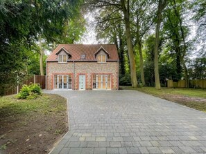 Une maison en pierre à deux étages, avec un toit en tuiles, une allée pavée et un jardin bien entretenu.