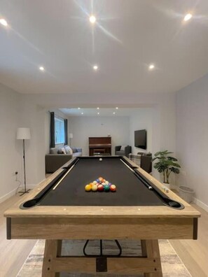 A pool table with balls in the center, a sofa, a TV, and a plant in a modern living room. - The Gatehouse & Lodge | Large Group Retreat (Holt)