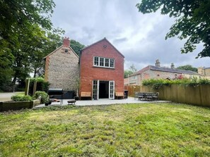 Een woonhuis met twee verdiepingen, een gevel van natuursteen en een aanbouw van baksteen.