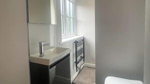 A modern bathroom with a white sink, dark cabinetry, a mirror, a window, and a white toilet. - The Gatehouse & Lodge | Large Group Retreat (Holt)