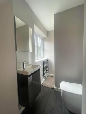 Een moderne badkamer met een witte wastafel, donkere kastjes, een spiegel, een raam en een wit toilet.
