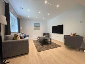 A modern living room with a grey sofa, a coffee table, and a grey armchair. - The Gatehouse & Lodge | Large Group Retreat (Holt)