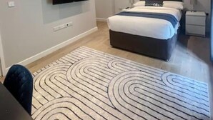A modern bedroom with a bed, a TV mounted on the wall, and a patterned rug. - The Gatehouse & Lodge | Large Group Retreat (Holt)