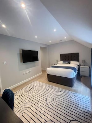 Een moderne slaapkamer met een bed, een aan de muur bevestigde televisie en een kamerkleed met een patroon.