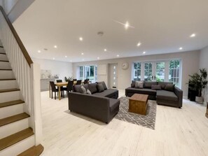 A spacious living room with two sofas, a coffee table, and a dining area with chairs and a table. - The Gatehouse & Lodge | Large Group Retreat (Holt)