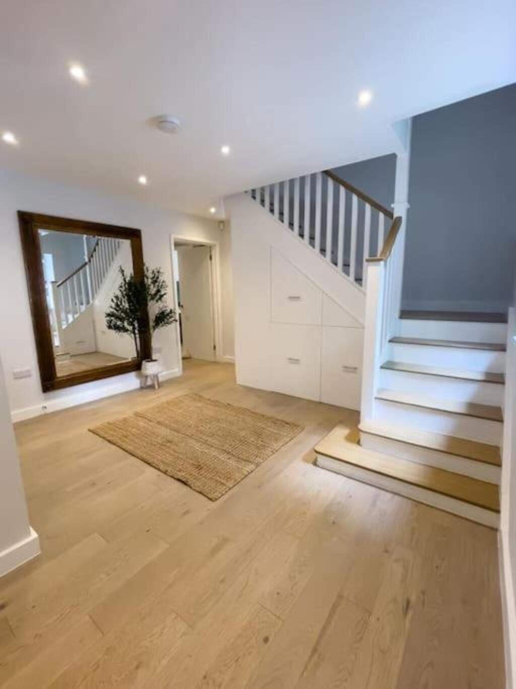 A spacious room with a wooden floor, a large mirror, a staircase, and a door leading to another area.