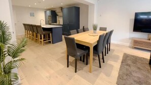 A modern living space with a dining area, kitchen, and a flat-screen TV. - The Gatehouse & Lodge | Large Group Retreat (Holt)