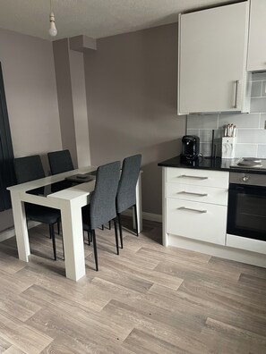Una cocina moderna con armarios blancos, encimera negra y un comedor con mesa blanca y sillas grises.