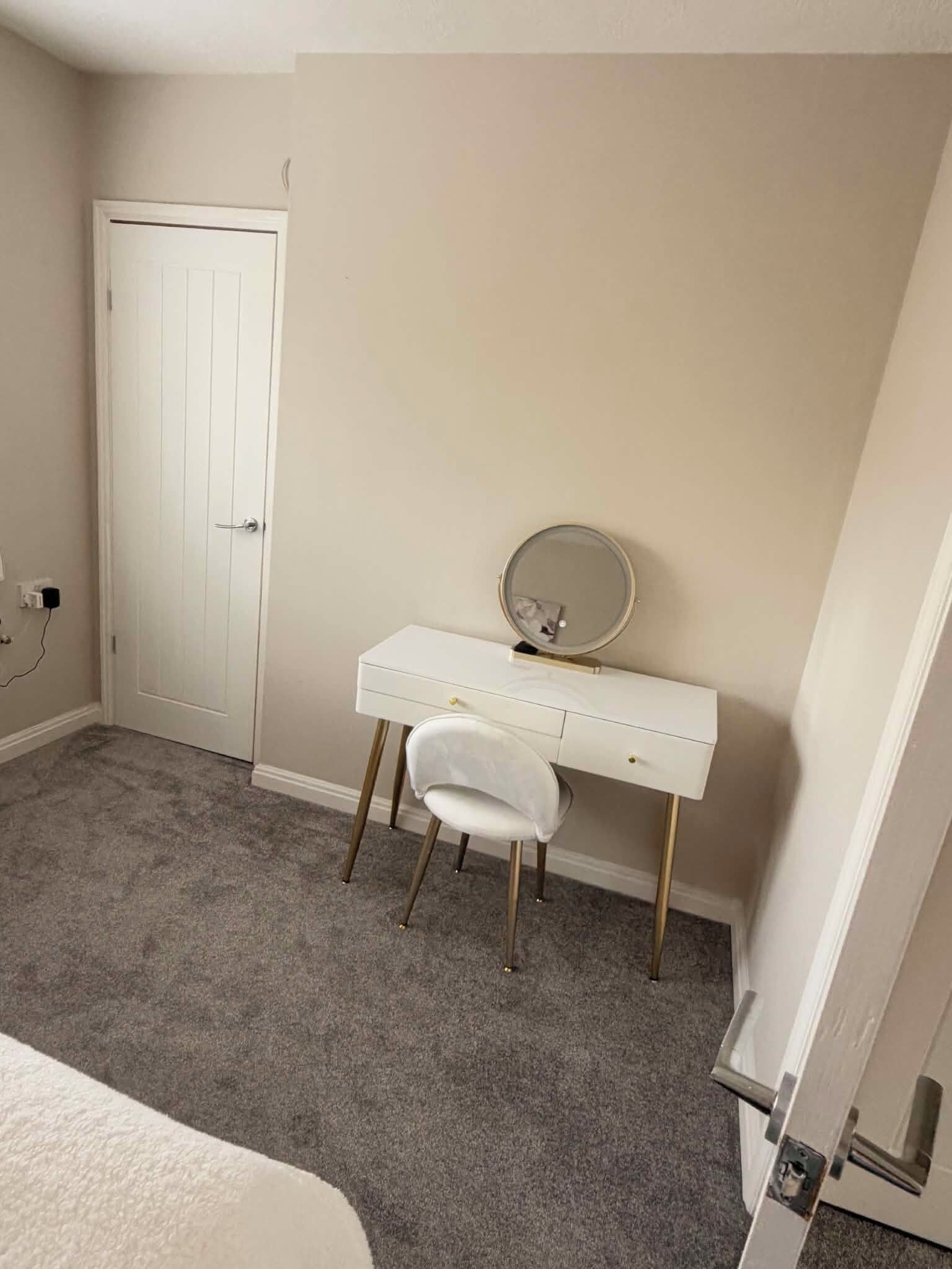 A bedroom with a white dresser, a round mirror, and a white chair.
