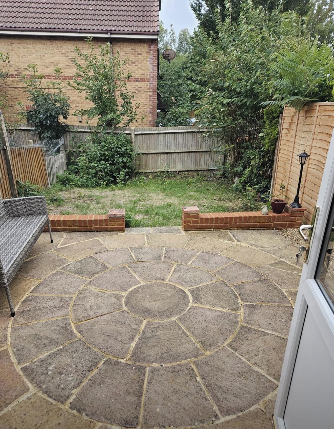 A patio with stone flooring, a wooden fence, and a brick wall.