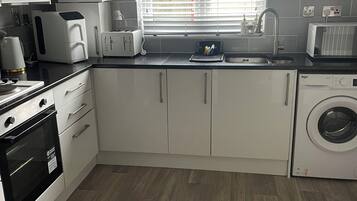 A modern kitchen with white cabinetry, a built-in oven, a microwave, a toaster, and a washing machine.