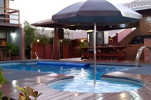 A swimming pool with a waterfall feature, surrounded by wooden decking and a covered seating area. - Recanto Reino Encantado 1 (Olímpia)