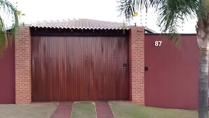 A closed wooden garage door with a brick wall and a number '87' on the right side. - Recanto Reino Encantado 1 (Olímpia)