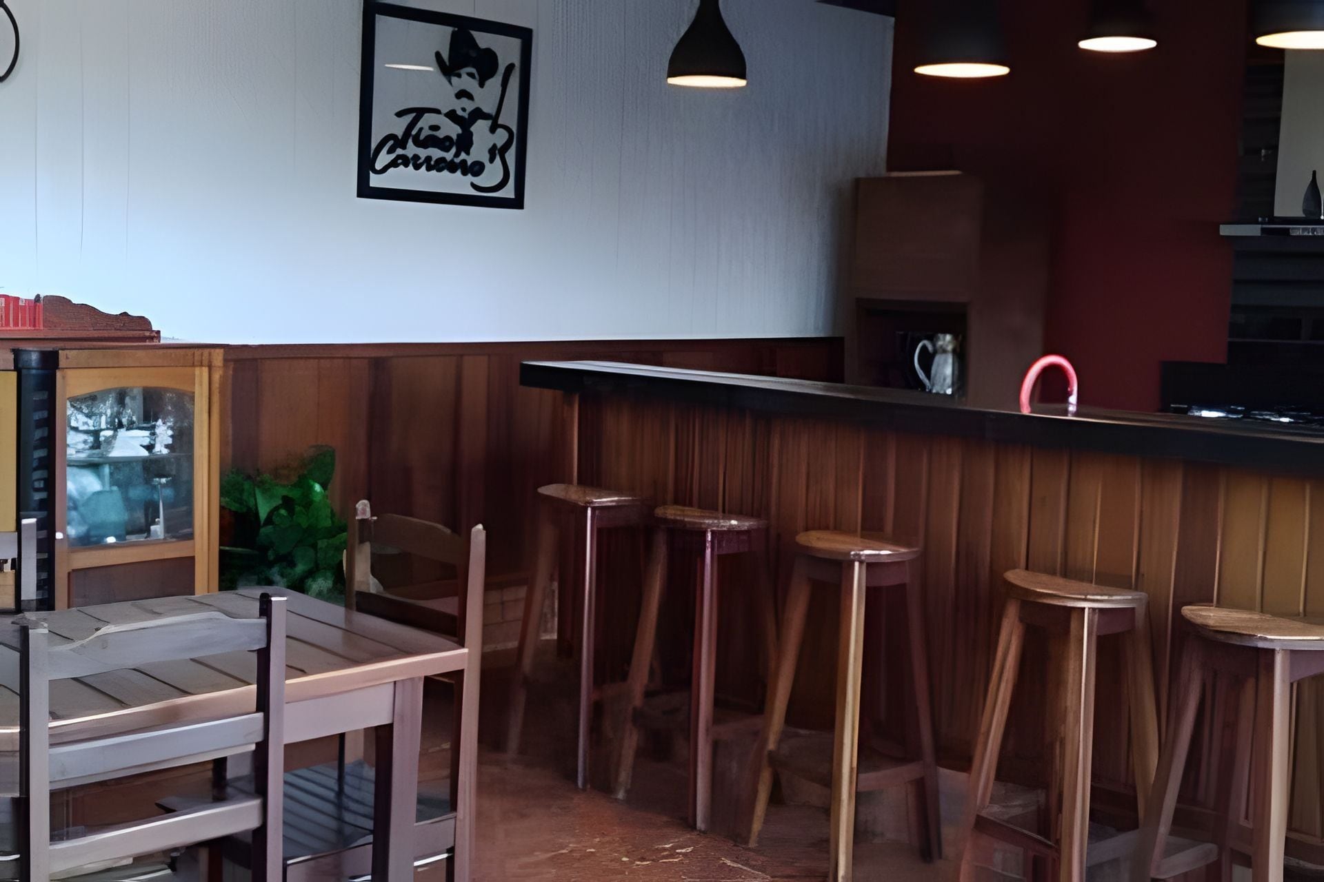 Eine Bar mit hölzernen Barhocker, einer Theke mit rotem Wasserhahn und einem gerahmten Bild an der Wand.
