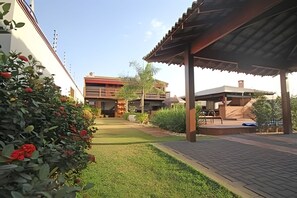 A courtyard with a paved walkway, a covered seating area, and a building with a flat roof. - Recanto Reino Encantado 1 (Olímpia)