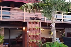 Edifici de diversos pisos amb façana de fusta, una escala i una palmera.