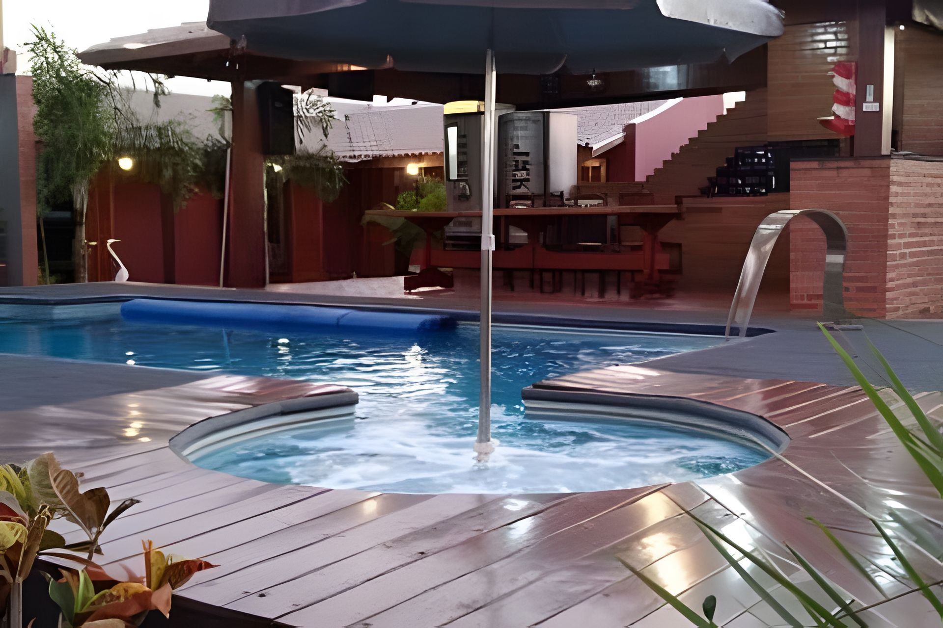 Uma área de piscina com hidromassagem, deck de madeira e espaço de estar coberto.